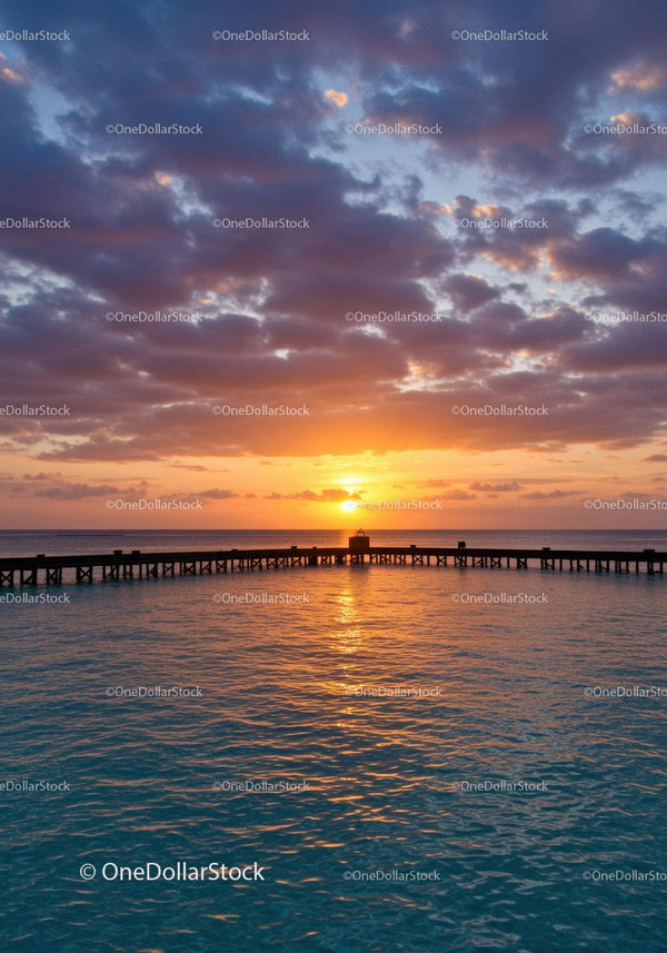 Sunset Over Calm Ocean with Wooden Pier and Cloudy Sky