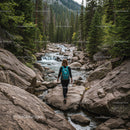 Woman Hiking Through Verdant Pine Forest Next to Mountain Stream