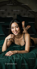 Smiling young woman relaxing on bed with green bedding
