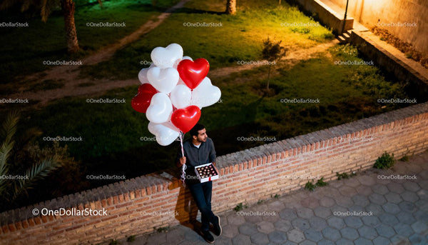 Man holding heart-shaped balloons and chocolates at night