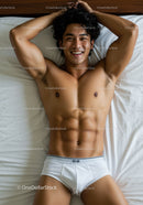Smiling fit young man relaxing on bed in white briefs