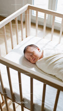 Newborn baby peacefully sleeping in wooden crib sunlight