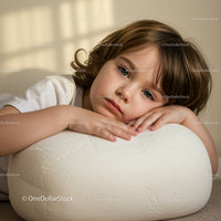 Thoughtful child resting head on soft white cushion