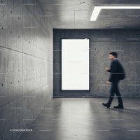 Man walking past illuminated blank poster in concrete corridor