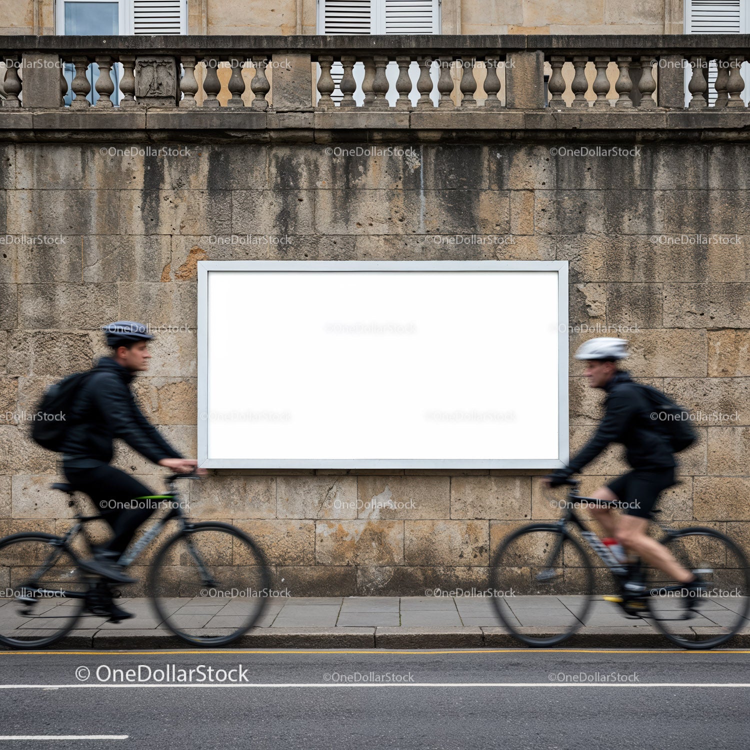 Dwóch rowerzystów przejeżdża obok pustego miejskiego billboardu na kamiennym murze