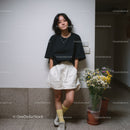 Casual Young Woman in Black T-Shirt and Beige Shorts Standing Indoors
