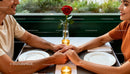 Couple holding hands over candlelit dinner table with rose