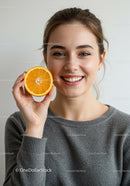 Young Woman Smiling with Fresh Orange Slice in Hand for Healthy Lifestyle