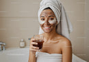 Young woman in towel wrap smiling with facial mask and eye patches