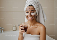 Young woman in towel wrap smiling with facial mask and eye patches
