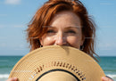 Smiling Woman Holding Straw Hat with Ocean View in Background