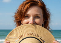 Smiling Woman Holding Straw Hat with Ocean View in Background