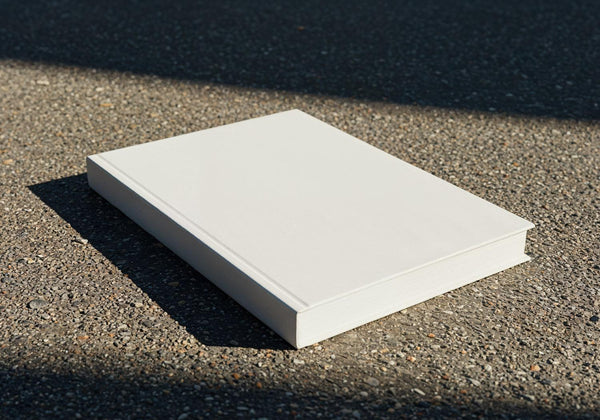 Blank white hardcover book on textured pavement surface JPG Mockup Image