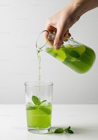 Pouring refreshing green mint drink into clear glass