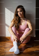 Young woman relaxing in pink activewear by sunlit wall