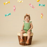Smiling toddler sitting on cupcake with hanging candies