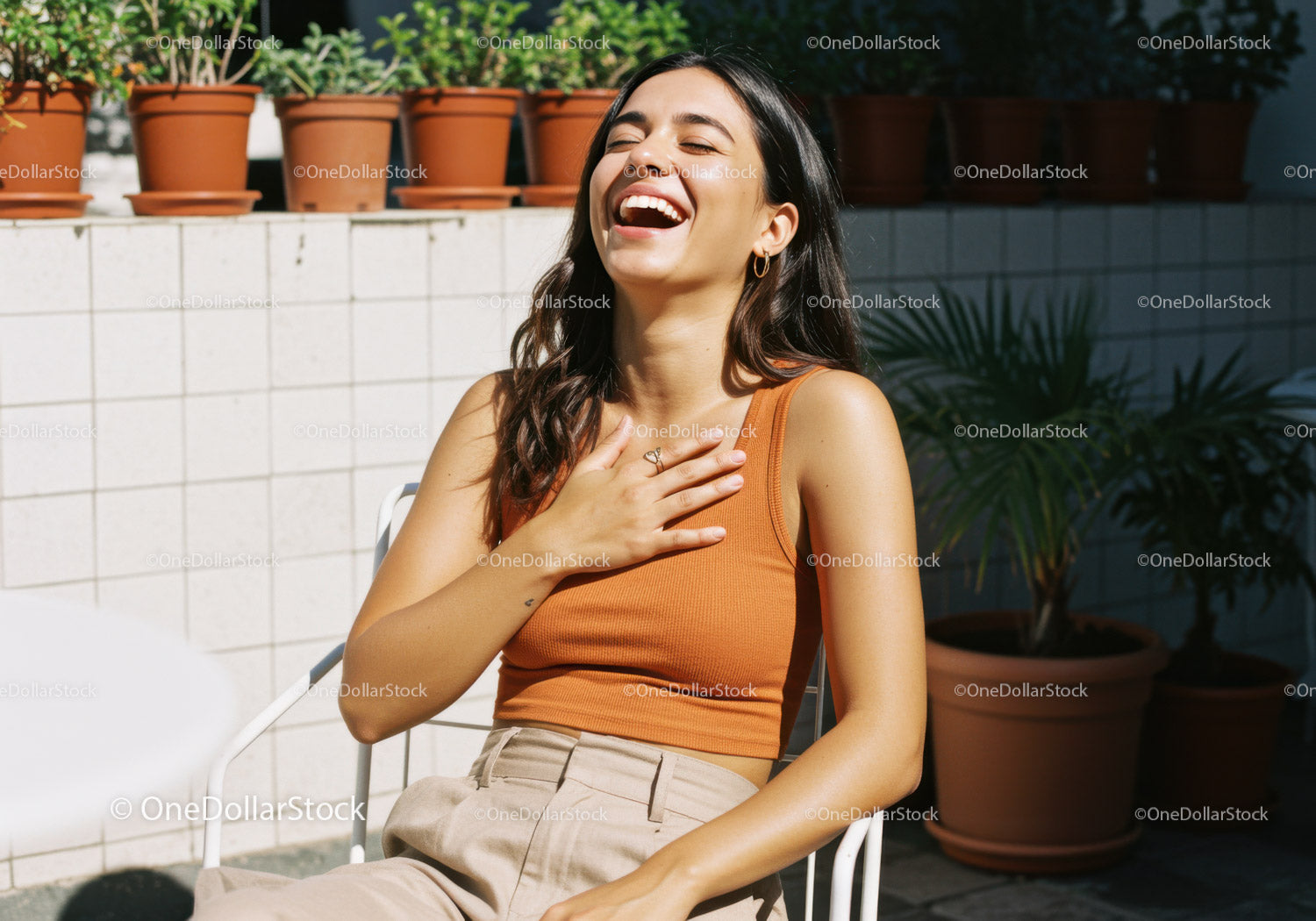 Happy Woman in Orange Tank Top Sitting Outdoors on Sunlit Terrace