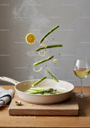 Fresh asparagus and lemon slices sizzling in white pan