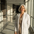 Senior Woman in White Coat Standing in Bright Modern Hospital Corridor