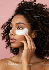 Beautiful Woman Applying Eye Patches with Curly Hair against Pink Background