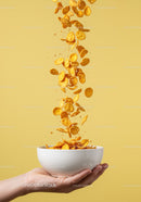 Hand Holding Bowl with Falling Cornflakes On Yellow Background
