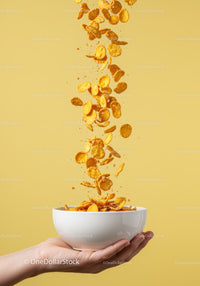 Hand Holding Bowl with Falling Cornflakes On Yellow Background
