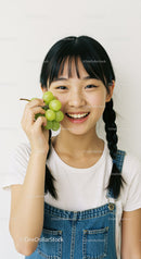 Young Girl with Black Hair Holding Fresh Green Grapes in Indoor Setting