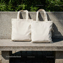 Two blank cotton tote bags resting on stone bench outdoors