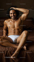 Relaxed muscular man smiling on brown bed in white briefs