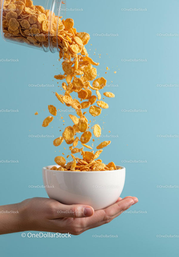 Pouring crunchy corn flakes into white bowl held by hand