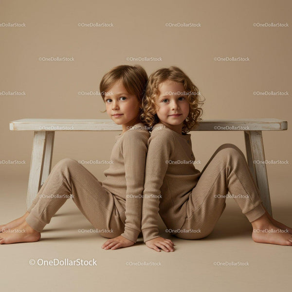 Two children sitting back to back in cozy beige outfits