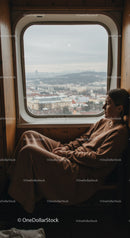 Contemplative Woman Sitting by Large Train Window Overlooking Cityscape