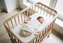 Newborn baby peacefully sleeping in wooden crib by window