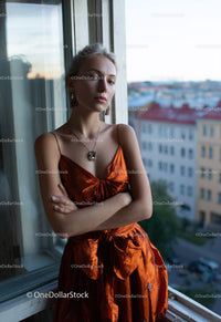 Elegant Woman in Orange Satin Dress by Window with City View