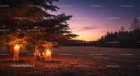 Two glowing candles under pine tree at dusk in open field