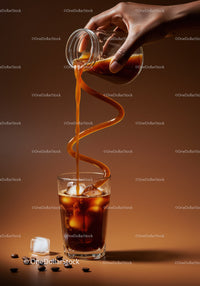 Iced coffee pouring in artistic swirl over ice cubes