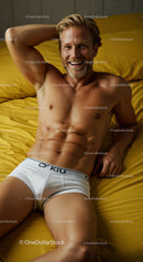 Smiling man relaxing on mustard bed in white underwear