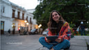 Young Woman Sitting Cross-Legged with Tablet in City Street Setting