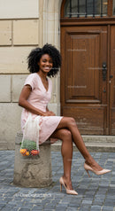 Happy woman in pink dress sitting outdoors with groceries