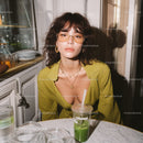 Fashionable woman with glasses and jewelry sitting with drink in cafe