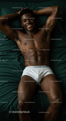 Smiling man relaxing in white briefs on dark green bedding