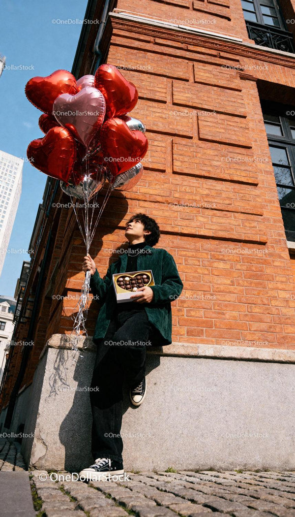 Young man holding heart balloons and chocolates outdoors