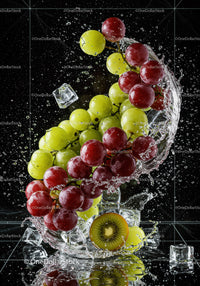 Fresh grapes and kiwi with ice splash on black