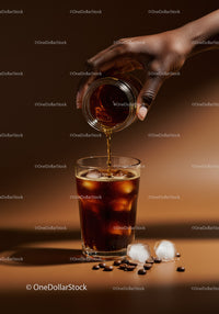 Pouring iced coffee over glass with ice cubes and beans