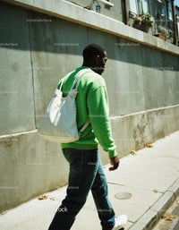 Young Man in Green Sweater Walking Through Urban Street Scene