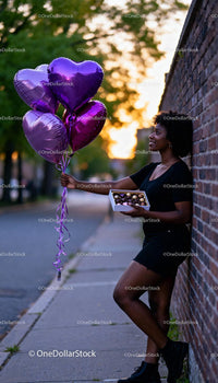 Smiling woman holding purple heart balloons and chocolates