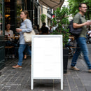 Blank sidewalk sign outside busy urban café