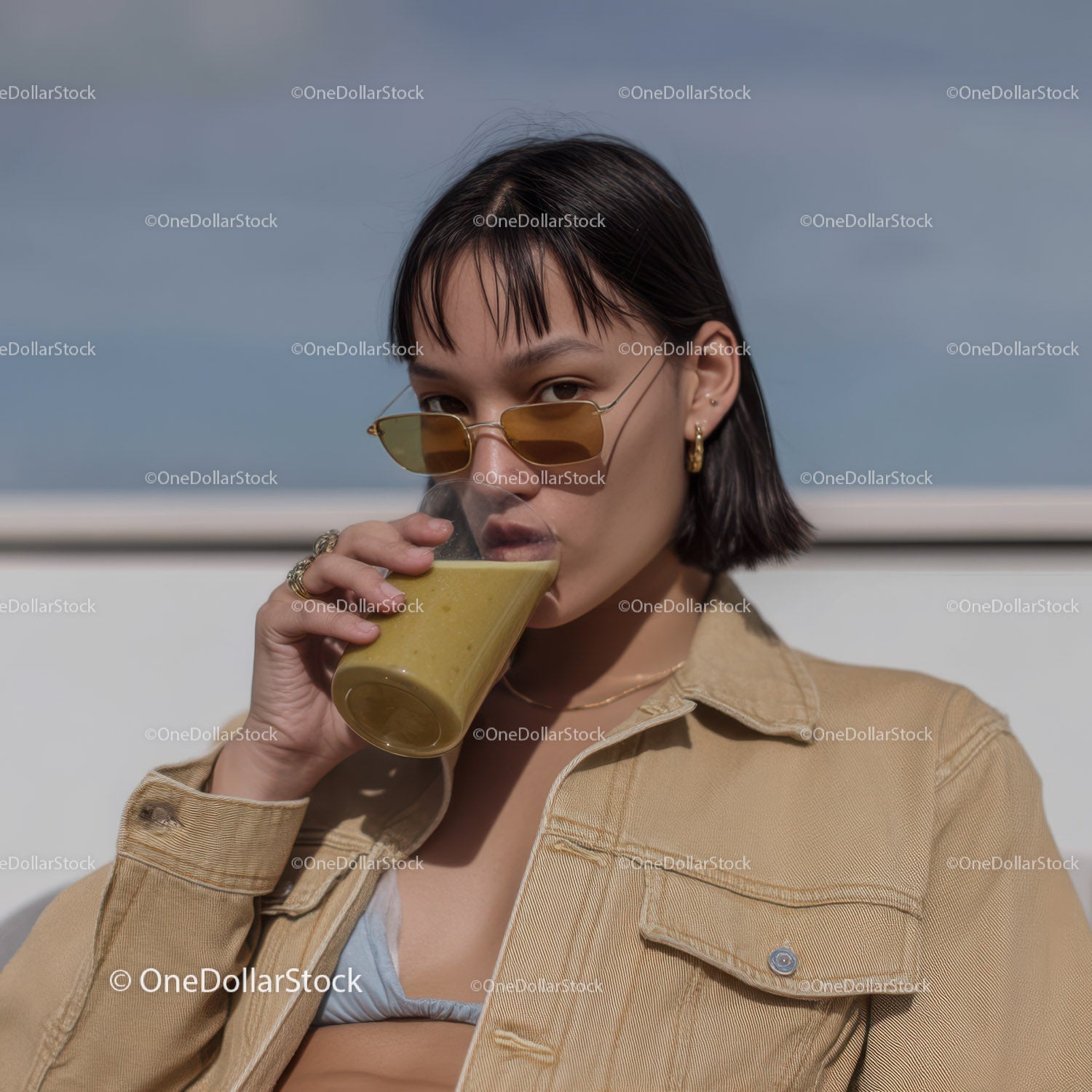 Stylowa kobieta pijąca smoothie na świeżym powietrzu pod błękitnym niebem