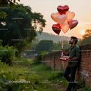 Man Holding Heart Balloons and Chocolates at Sunset