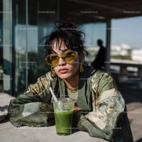 Fashionable woman with curly hair and yellow sunglasses sitting outdoors
